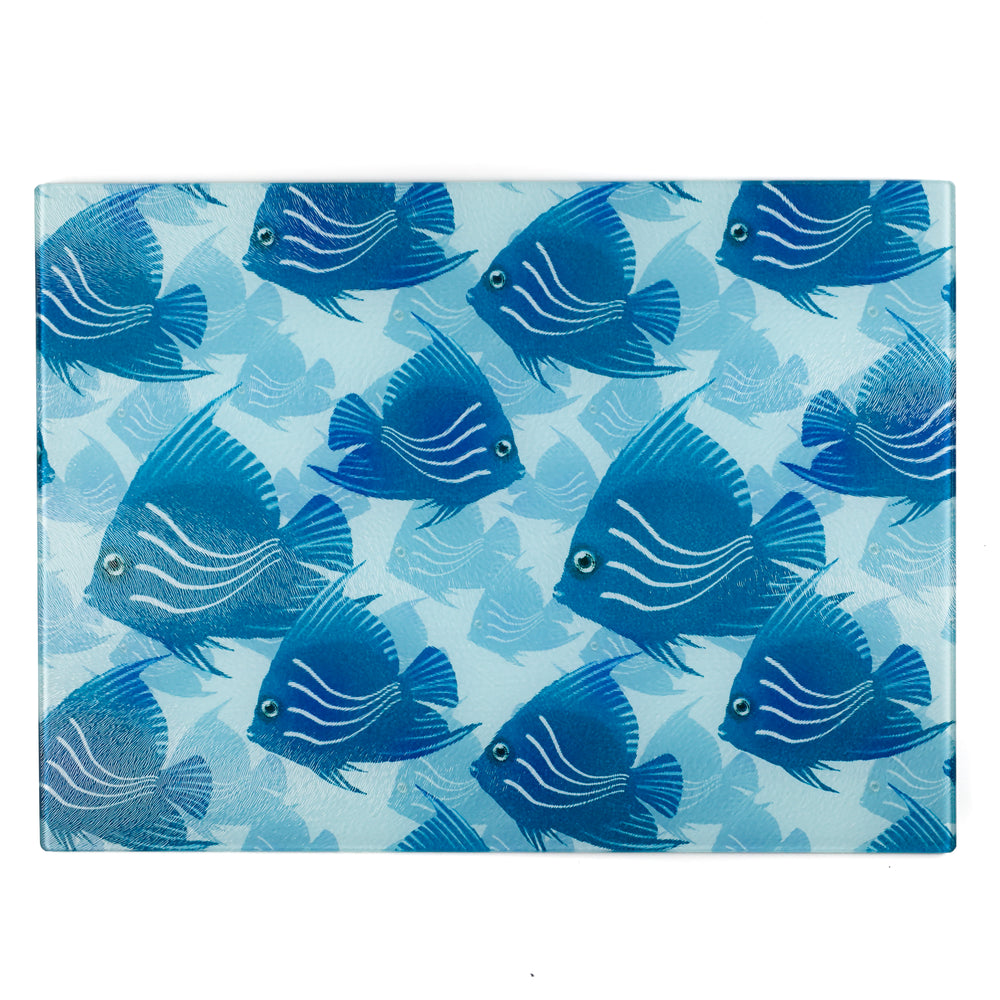A rectangular glass cutting board with a pattern of hand-drawn blue and turquoise angel fish on a blue grey sea background.