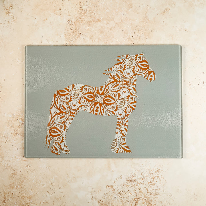 A grey glass worktop protector with a brown horse design on it, placed on a marble surface.