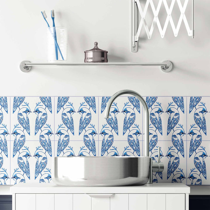 Bathroom with blue and white bird pattern on tiles, silver faucet, and white cabinets.