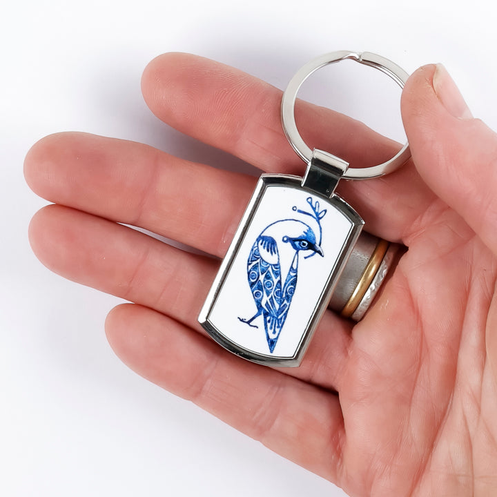 A metal keyring with a millefiori print inlay featuring blue and white lovebirds held in a hand