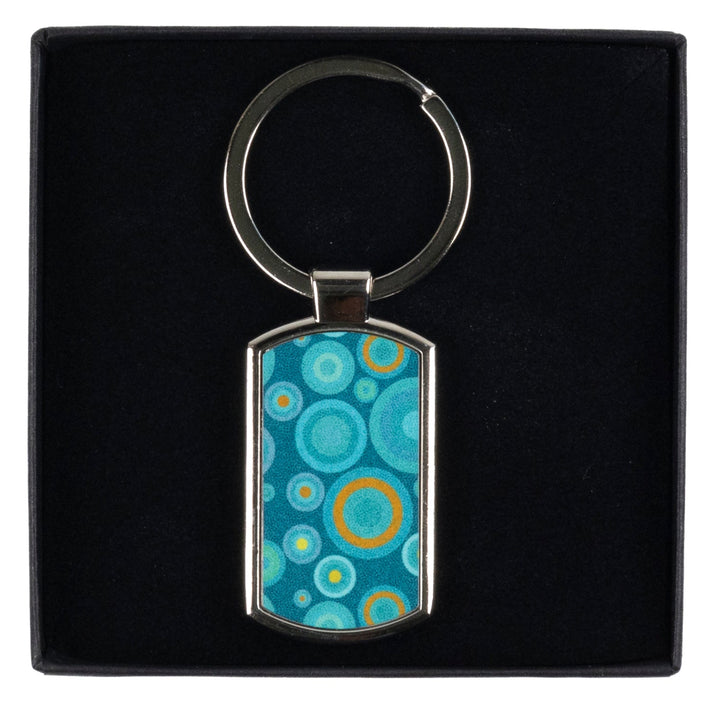 A metal keyring with a blue millefiori print inlay, presented on a black DoodlePippin box with a velvet liner.